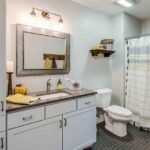 Small bathroom storage ideas for renters showing an over-toilet étagère, ladder shelf, and rolling cart in a warm neutral rental bathroom