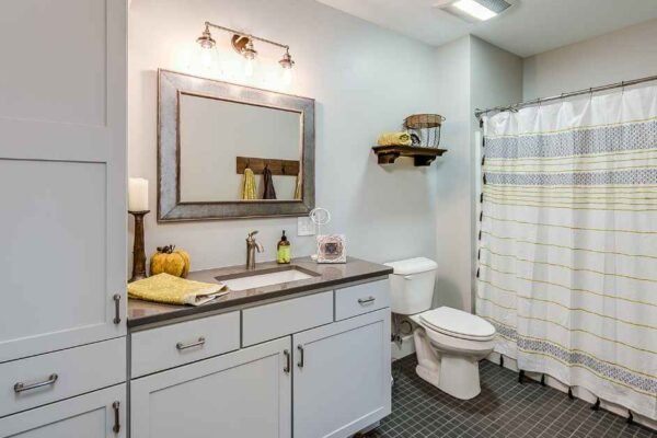 Small bathroom storage ideas for renters showing an over-toilet étagère, ladder shelf, and rolling cart in a warm neutral rental bathroom