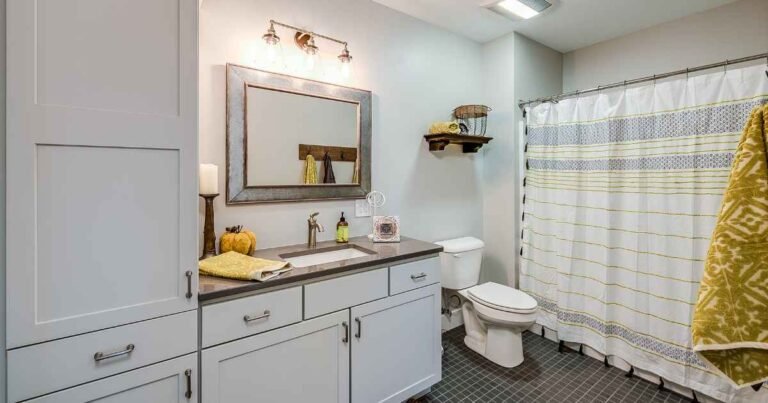 Small bathroom storage ideas for renters showing an over-toilet étagère, ladder shelf, and rolling cart in a warm neutral rental bathroom