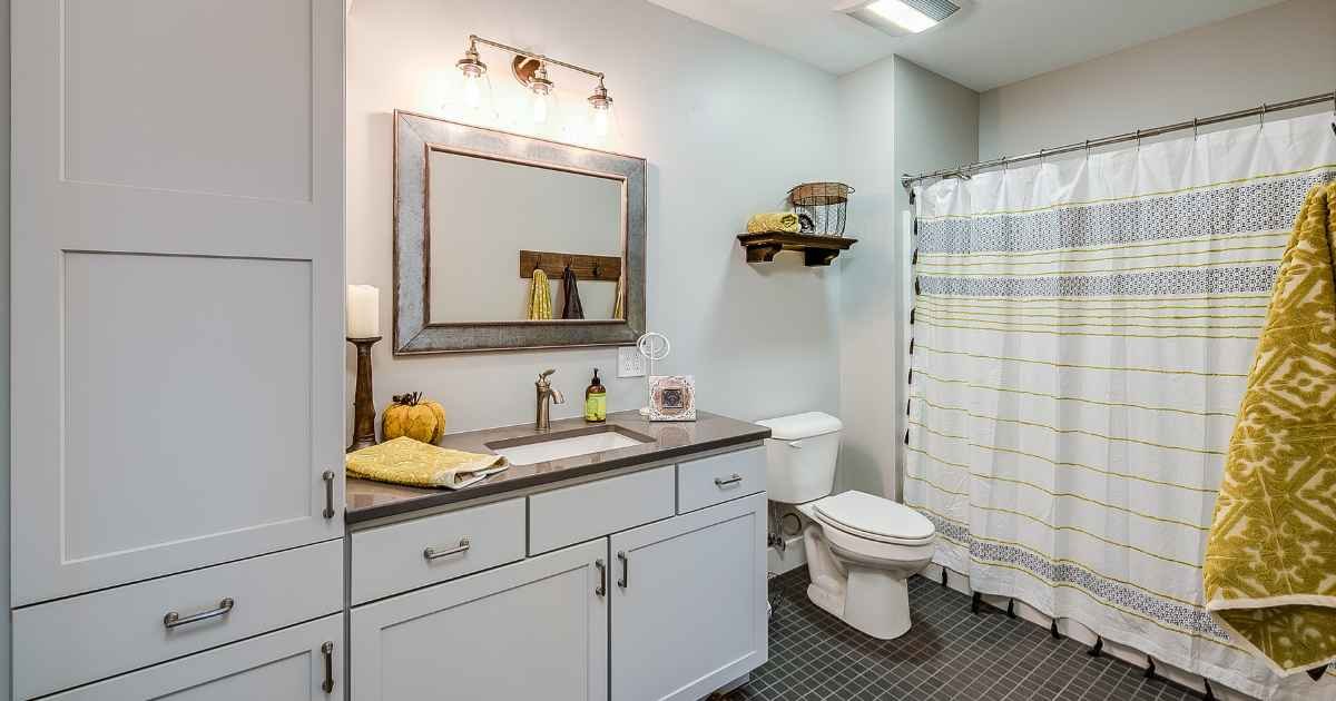 Small bathroom storage ideas for renters showing an over-toilet étagère, ladder shelf, and rolling cart in a warm neutral rental bathroom